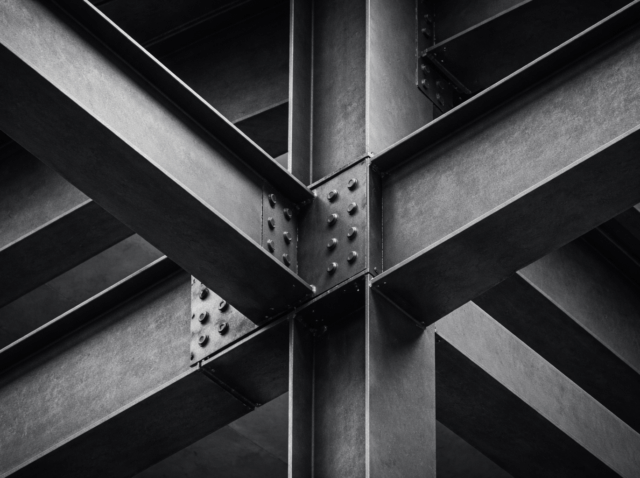 Abstract close-up of intersecting steel beams illustrating commercial intelligence as decision infrastructure that supports coordinated B2B growth.